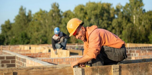 Two construction workers focusing on creating wooden structures outdoors in a sunny setting., tags: bauen mit die der - pexel