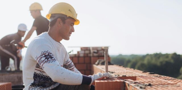 Construction worker laying bricks outdoors in sunny weather with lush greenery in background., tags: wenn bauschaffende aufbau - pexel